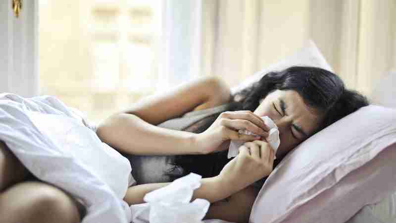 A woman lying in bed sneezing, illustrating symptoms of a cold or flu., tags: atemwegserkrankungen - pexel